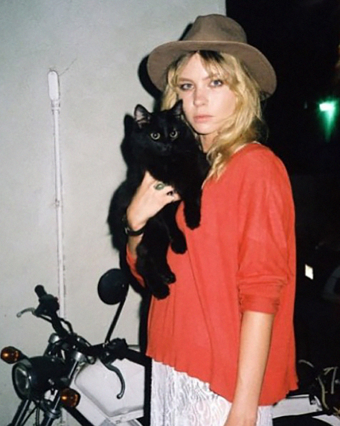 The Lilo & Stitch actress with blonde hair and a hat, holding a black cat. A motorcycle is in the background.