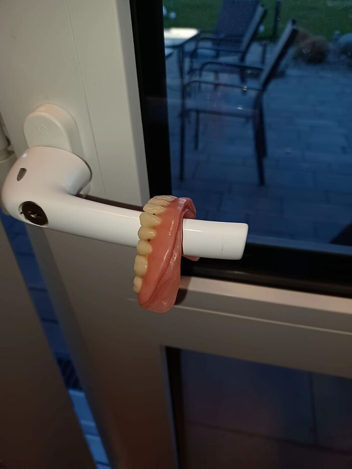 A bizarre image of dentures hanging on a white door handle, making viewers question reality.