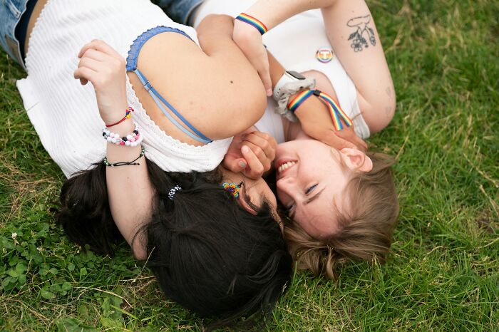 Two women lying on grass wearing rainbow accessories