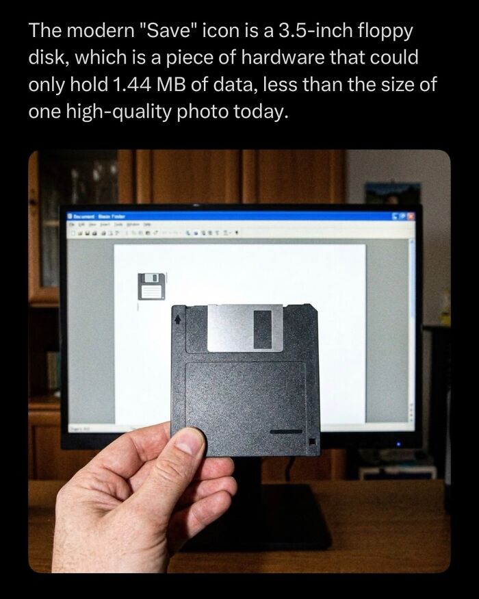 Hand holding a 3.5-inch floppy disk save icon in front of a computer screen