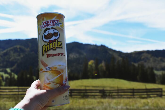 Hand holding Pringles Emmental flavor can against mountain landscape