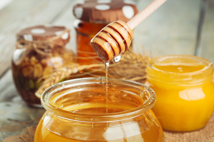 Honey dripping from wooden dipper into jar with jars of honey behind