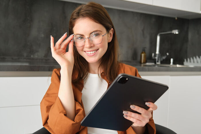 Smiling woman with glasses holding tablet in modern kitchen