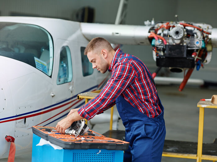 Man in blue overalls working on small airplane engine in hangar
