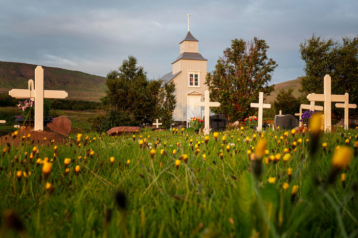 Grassy cemetery with white crosses and a small church in background under cloudy sky