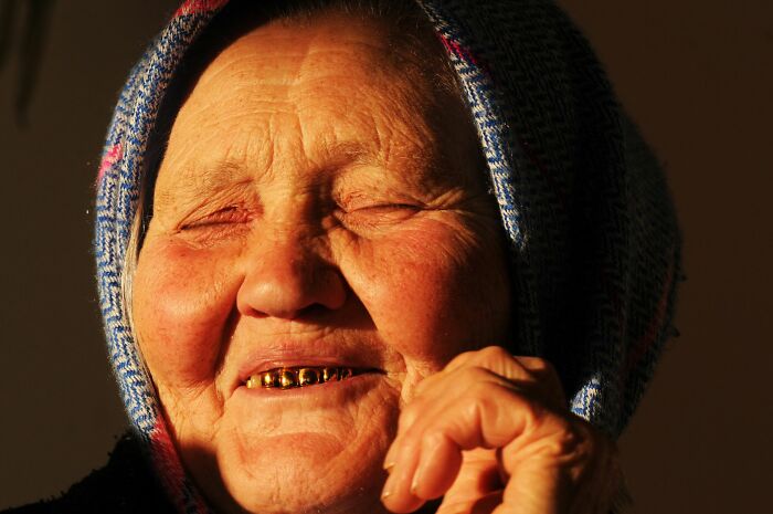 Elderly woman smiling with gold teeth wearing headscarf in warm sunlight