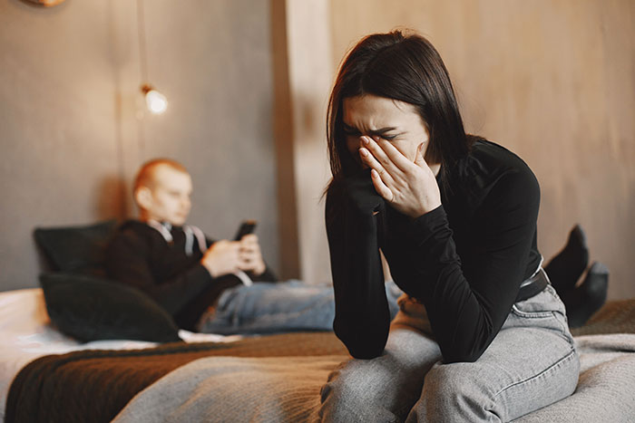 Woman distressed on bed with partner ignoring her, highlighting red flags women missed after wedding
