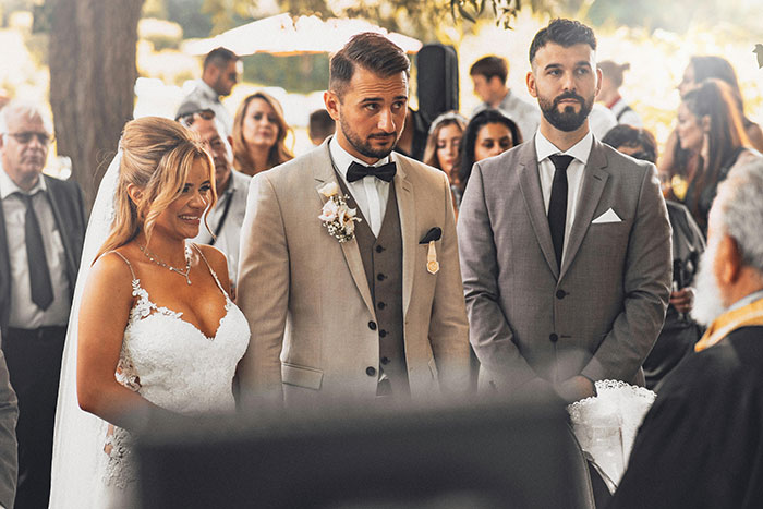 Bride and groom standing at wedding ceremony with best man and guests in background
