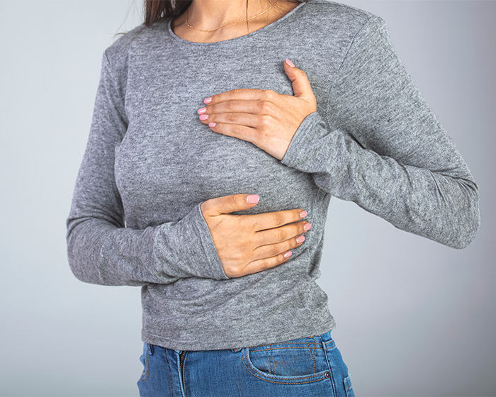Woman clutching her chest, experiencing discomfort, likely related to Sadness Trigger Syndrome distressing women.