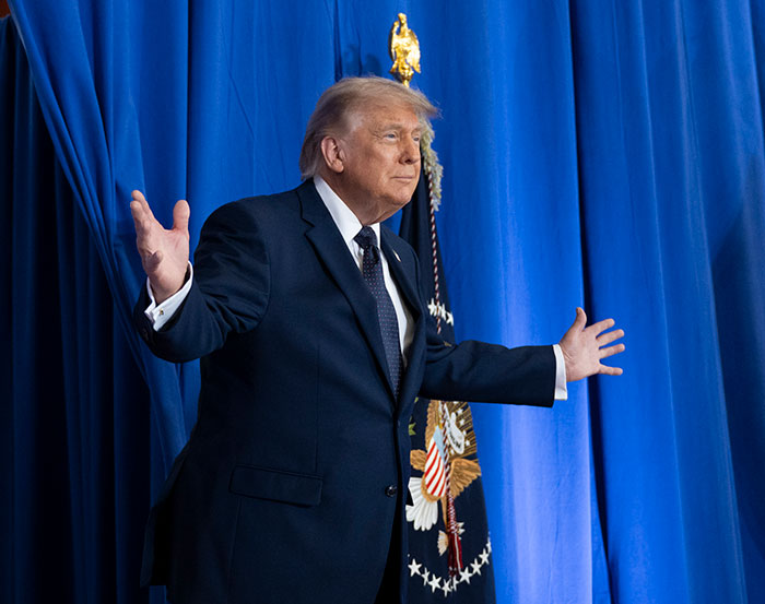 Donald Trump speaking at event with presidential flag and blue curtain backdrop