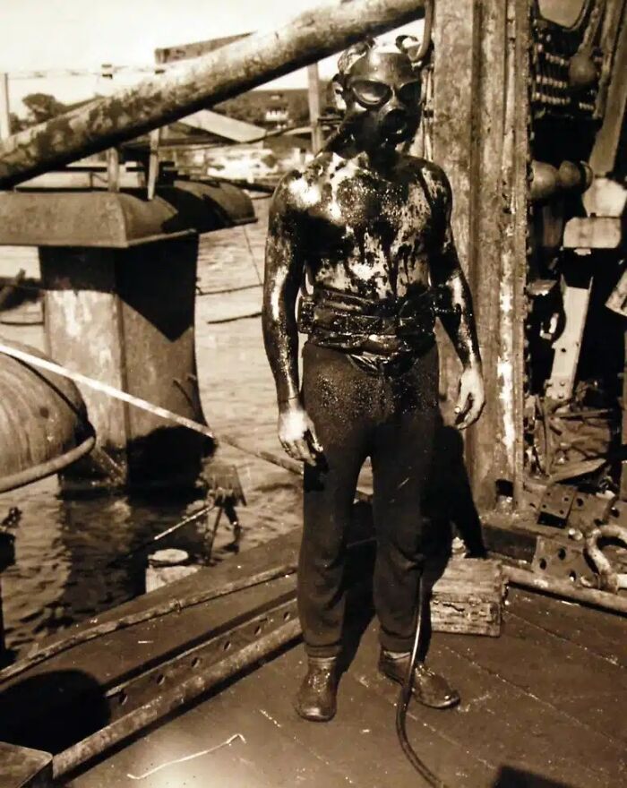 A man in diving gear, covered in oil, on a ship deck, one of many historical photos.