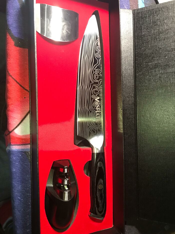 A high-quality chef knife with a decorative blade and a sharpener in a red and black box, ready for use by teachers or students.