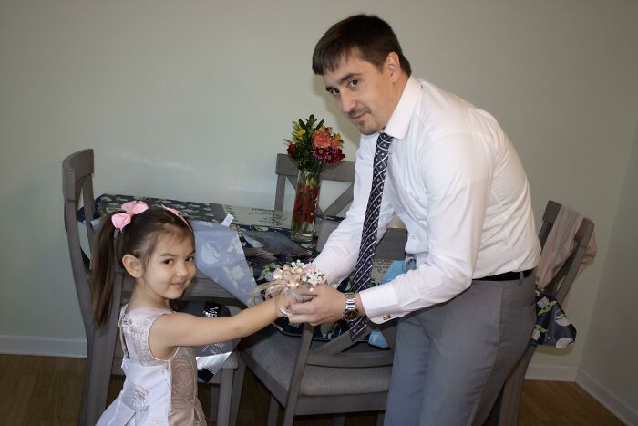 A father helps his young daughter put on a wrist corsage, a tender moment illustrating a beautiful adoption story.
