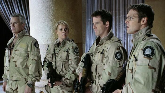 Stargate team in desert military uniforms holding weapons indoors Stargate team in desert military uniforms holding weapons indoors