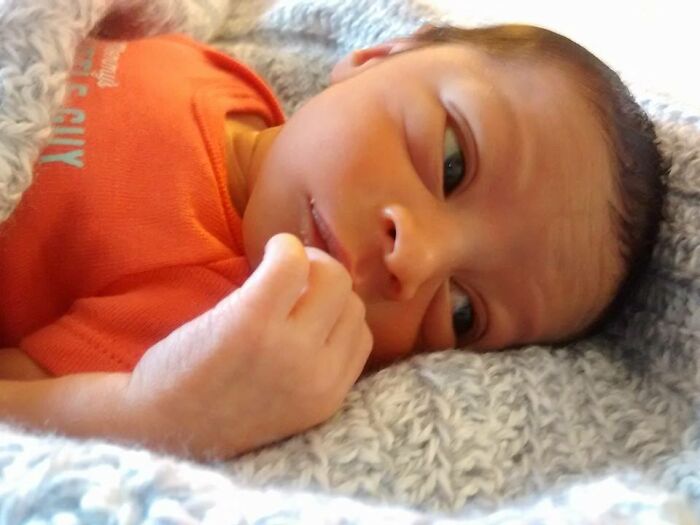 A close-up of an infant in an orange onesie looking at the camera, illustrating adoption stories.
