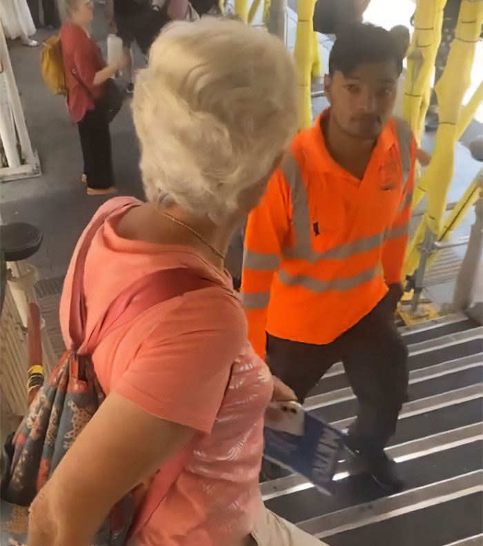 An 80YO woman on a public staircase, a man in an orange shirt passing by as a male Karen films her.