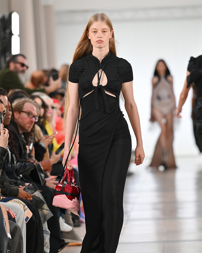 Vivian Musk walking on runway wearing long black dress and carrying purse Vivian Musk walking on runway wearing long black dress and carrying purse