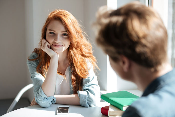 Red-haired woman smiling at a man during a workplace conversation Red-haired woman smiling at a man during a workplace conversation