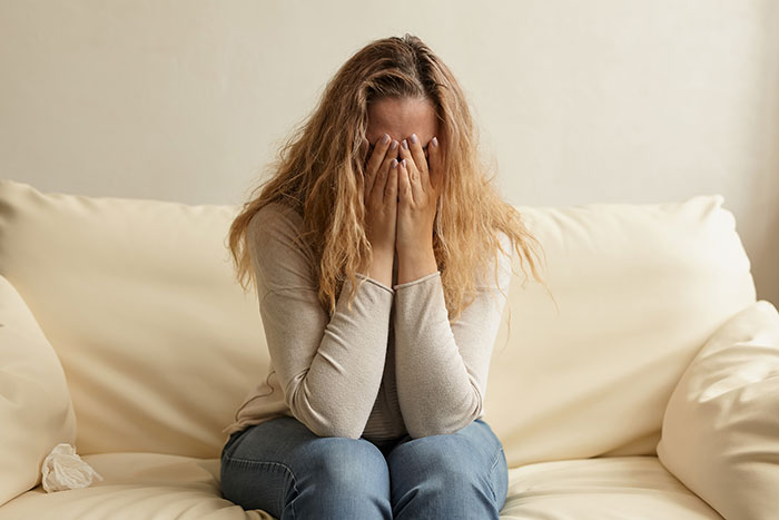 Woman sitting on couch covering her face in distress about wedding issues