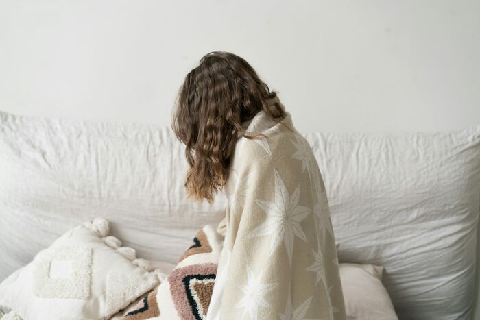 Sad woman wrapped in blanket sitting on couch indoors
