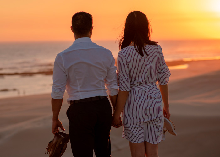 Couple holding hands on beach at sunset depicting modern dating and spoiled pig syndrome