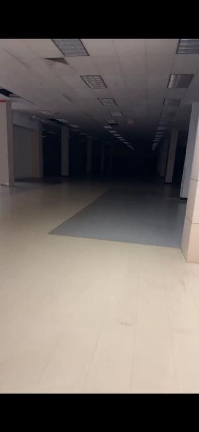 Deserted, dimly lit abandoned mall interior, an eerie liminal space.