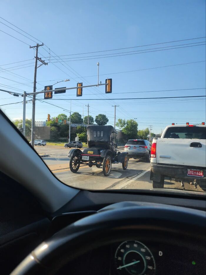 A bizarre image of a vintage car driving on a modern road, surrounded by contemporary vehicles.