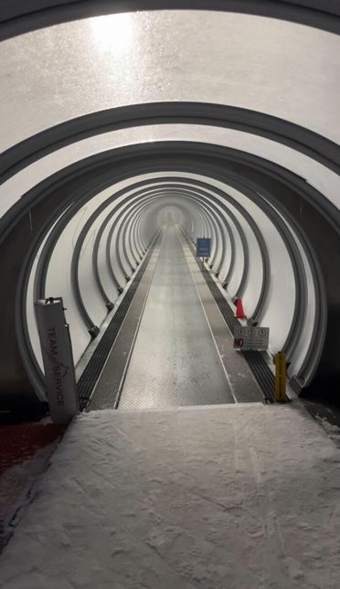 A long, snow-covered tunnel with a moving walkway, creating a haunting and endless liminal space.