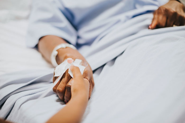 Person holding hand of patient with IV in hospital bed showing family conflict Person holding hand of patient with IV in hospital bed showing family conflict