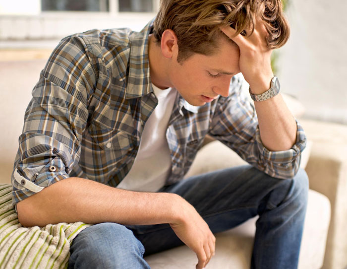 Young man looking distressed on couch about family issues Young man looking distressed on couch about family issues