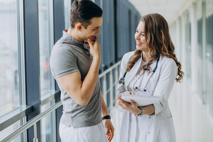 Young doctor talking and smiling with a male patient in a hospital hallway Young doctor talking and smiling with a male patient in a hospital hallway