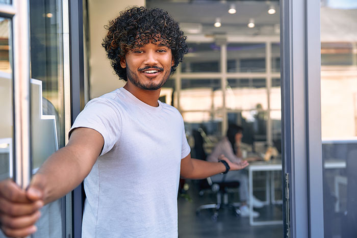 Man opening door with welcoming gesture illustrating stranger kindness