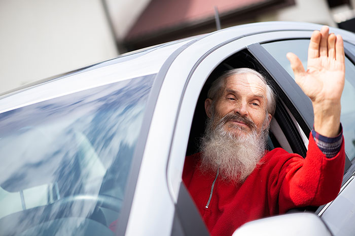 Elderly man in red sweater waving from car window showing kindness between strangers
