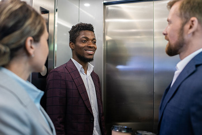 Smiling man socializing with colleagues inside elevator