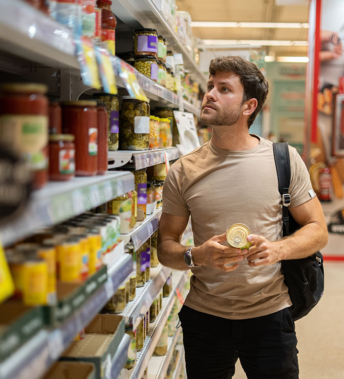 Man shopping in grocery aisle holding a can and reading label