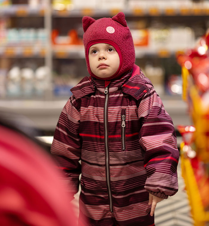 Child in warm striped coat and red hat standing indoors