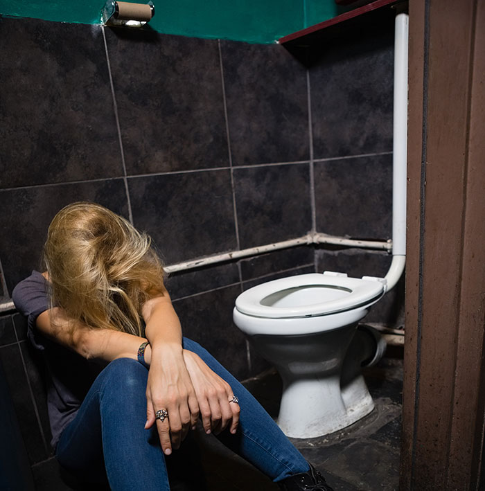 Person sitting on bathroom floor looking upset, reflecting unwritten rules between strangers