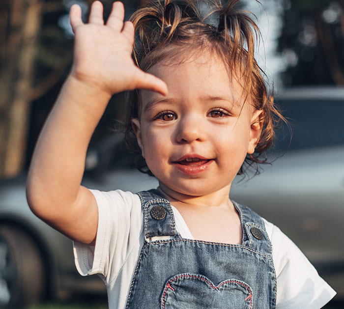 Toddler waving hand outdoors, representing unwritten rules between strangers