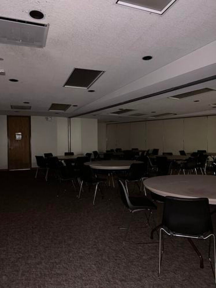 A dark, empty conference room with many round tables and chairs, an example of haunting liminal spaces.