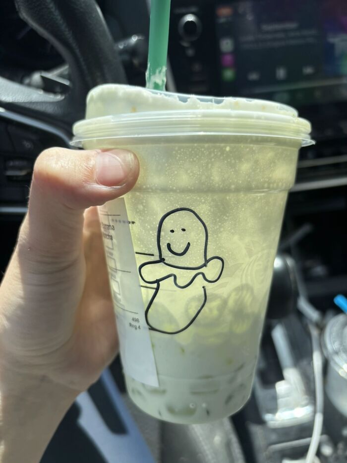 A hand holding a plastic cup with a bizarre drawing of a smiling creature, filled with a green drink.