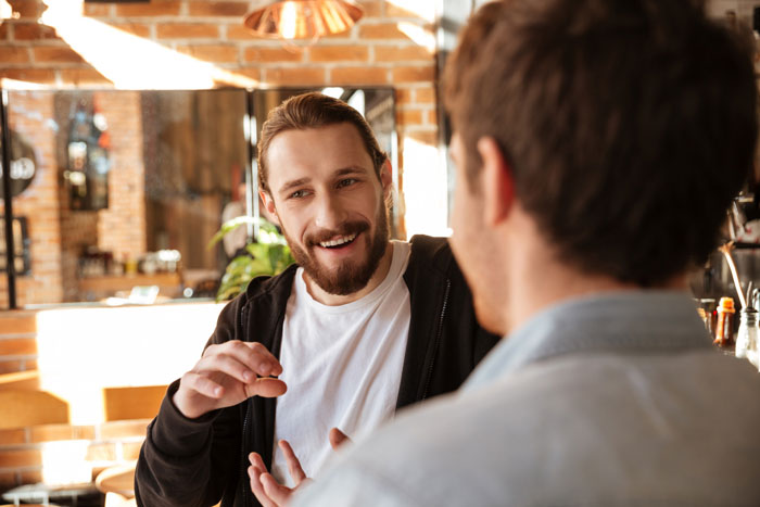 A talkative fiancé smiles happily, talking and gesturing to a stranger in a bustling cafe, craving attention. A talkative fiancé smiles happily, talking and gesturing to a stranger in a bustling cafe, craving attention.