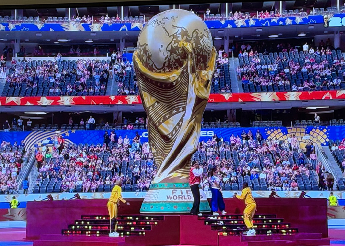 Large FIFA World Cup trophy on display with crowd in stadium seats