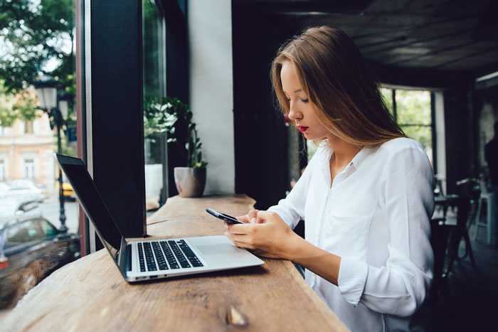 Woman texting on phone by window with laptop, couple argument theme Woman texting on phone by window with laptop, couple argument theme