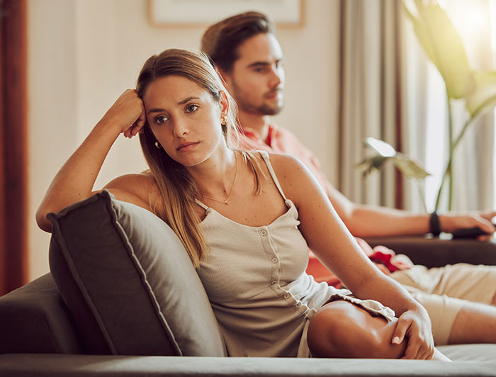Woman looking upset while sitting on couch with man, stressed about wedding excitement Woman looking upset while sitting on couch with man, stressed about wedding excitement
