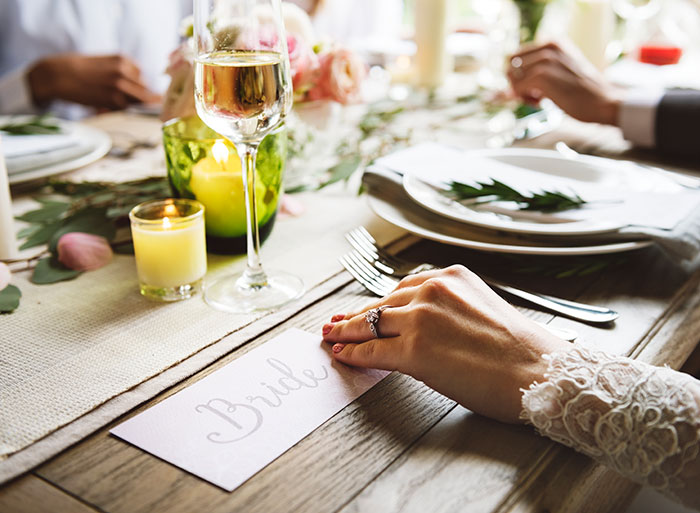 Bride wearing wedding ring at table with wedding place card and wine glass Bride wearing wedding ring at table with wedding place card and wine glass
