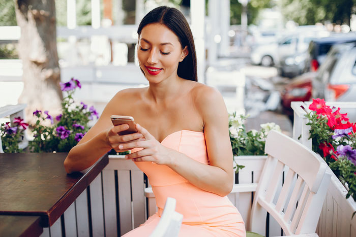 A woman in an orange dress smiles while looking at her phone at an outdoor cafe, representing the woman getting payback on her selfish friend. A woman in an orange dress smiles while looking at her phone at an outdoor cafe, representing the woman getting payback on her selfish friend.