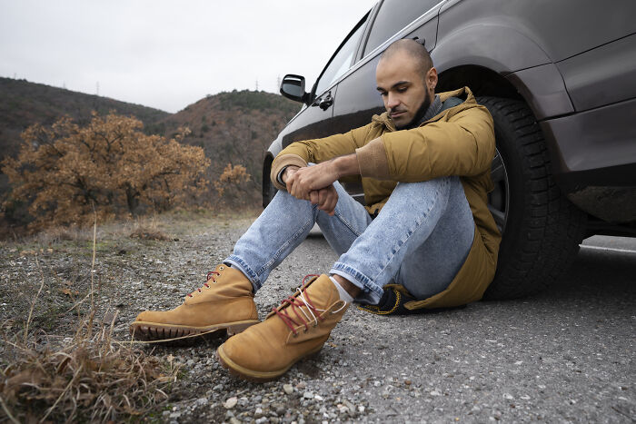 Man sitting by roadside with car trouble needing pure generosity help