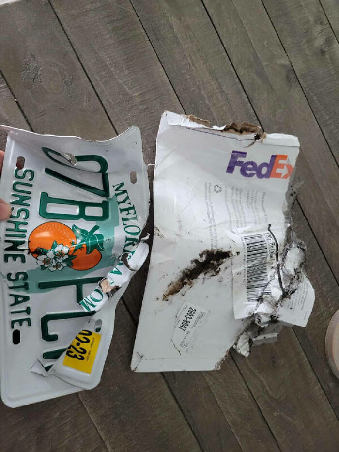 A damaged FedEx package and a bent license plate lie on a wooden floor, highlighting a severe delivery fail.