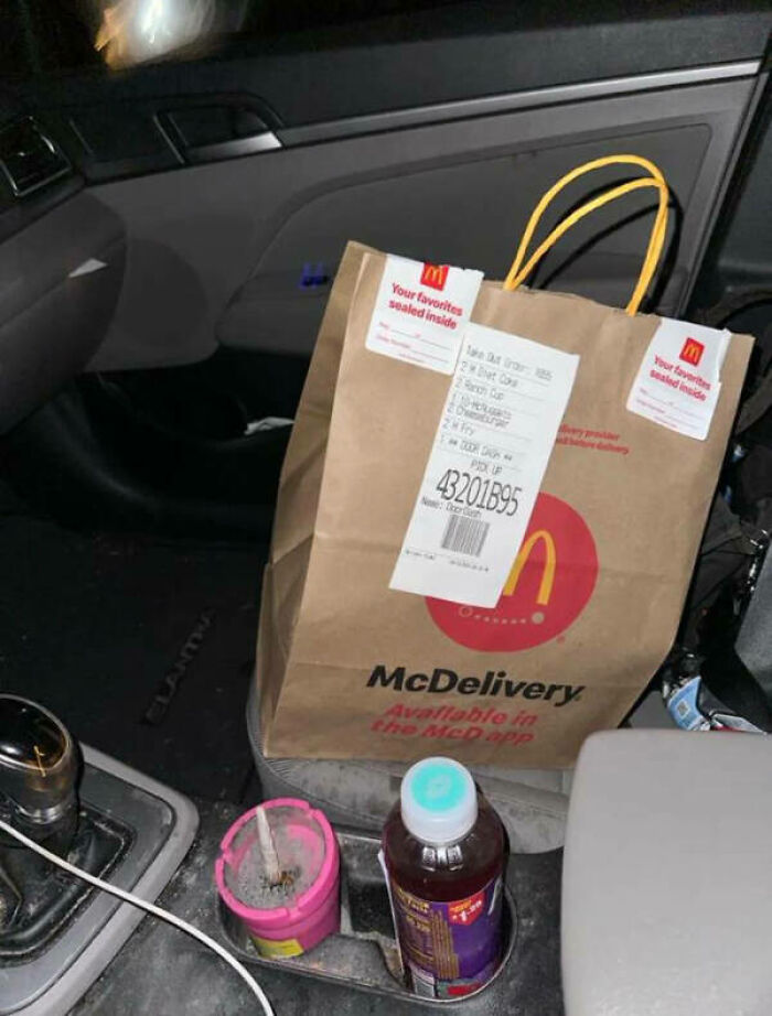A McDonald's delivery bag, a delivery fail, sits in a car's passenger seat next to a drink and an ashtray.