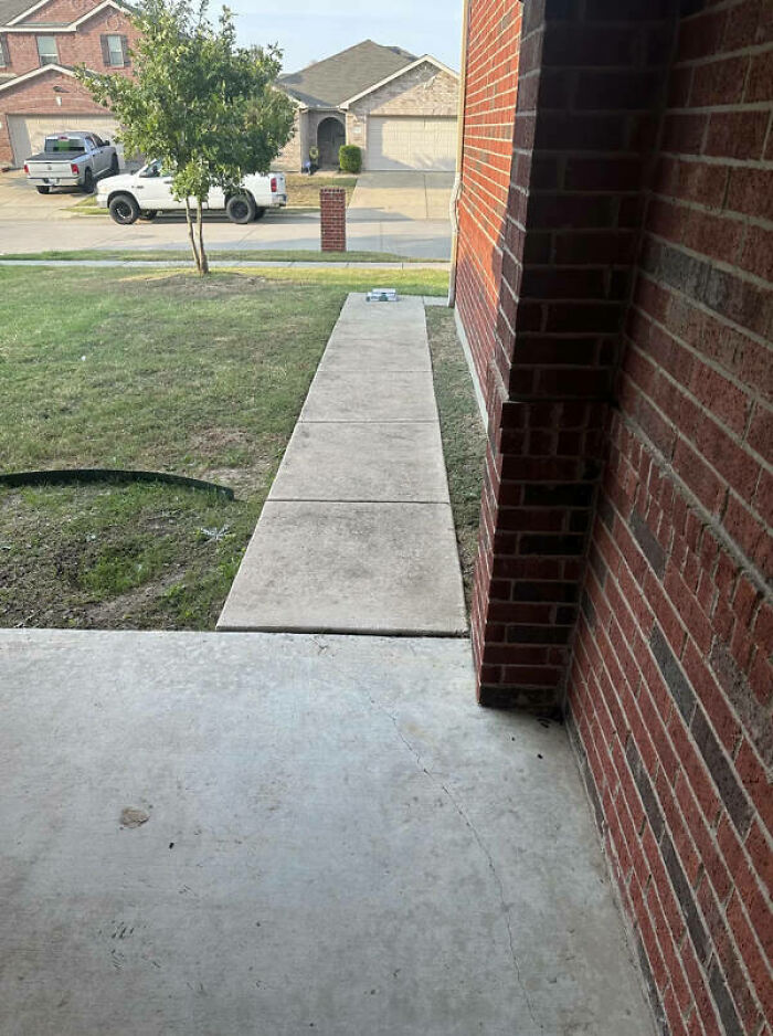 A long, narrow concrete path leading to a front door with a small package at the end of the path, depicting a delivery fail.